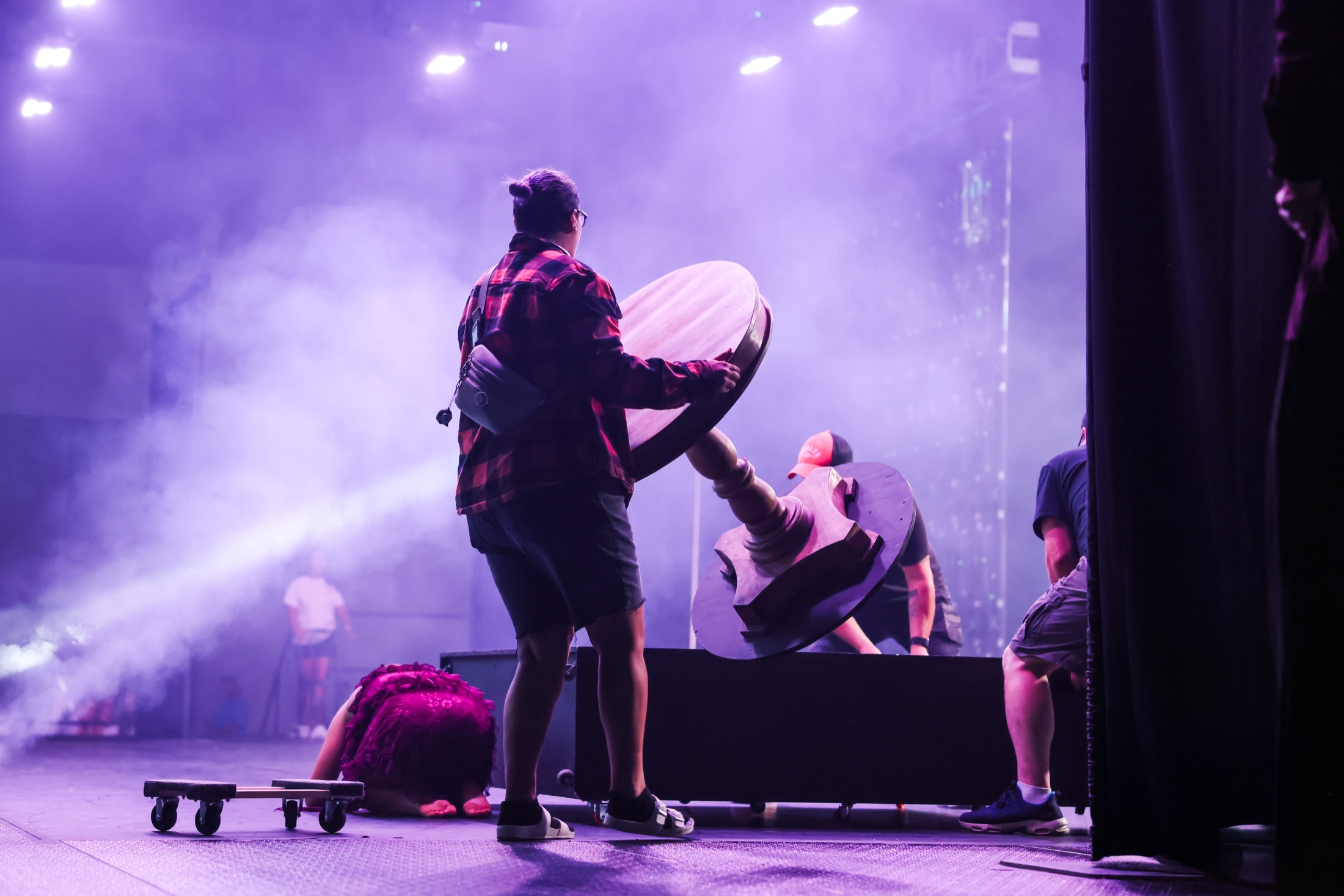 Crew members resetting props on a purple-lit stage between routines